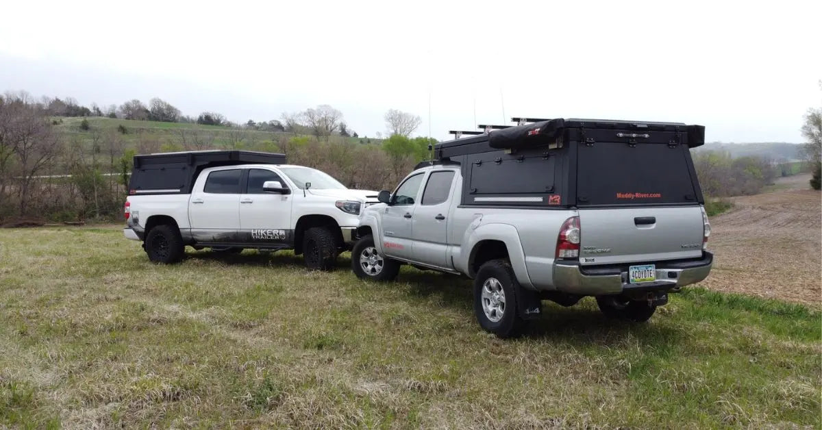 Two overland pickup trucks with camper toppers parked in a grassy field, showcasing truck camping in Texas with off-road setups and gear storage.