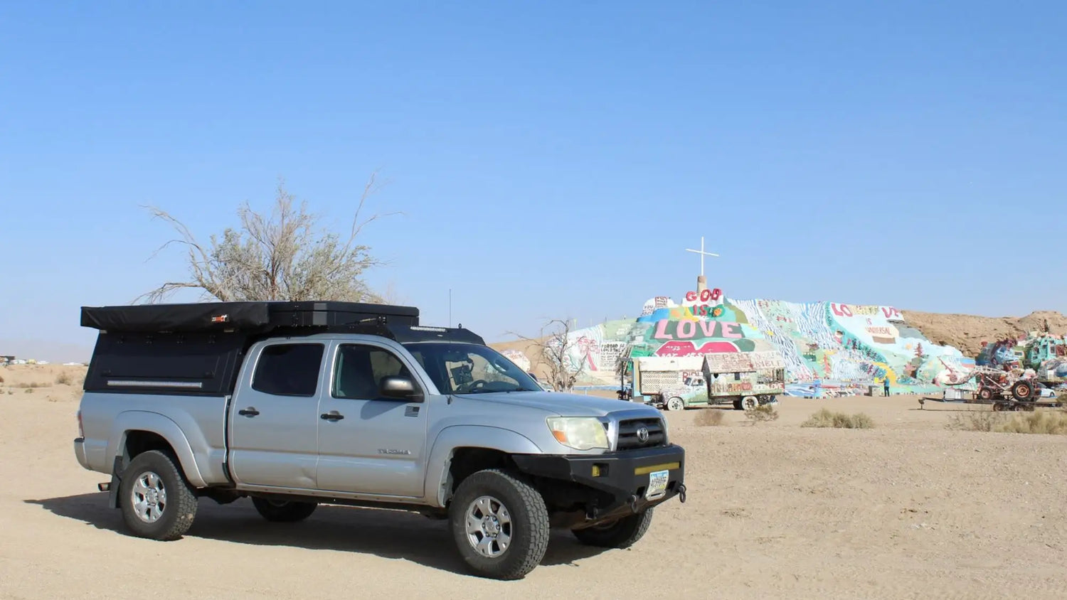 Comparison of truck topper vs rooftop tent showing a pickup equipped with a low-profile topper in a desert camping environment.