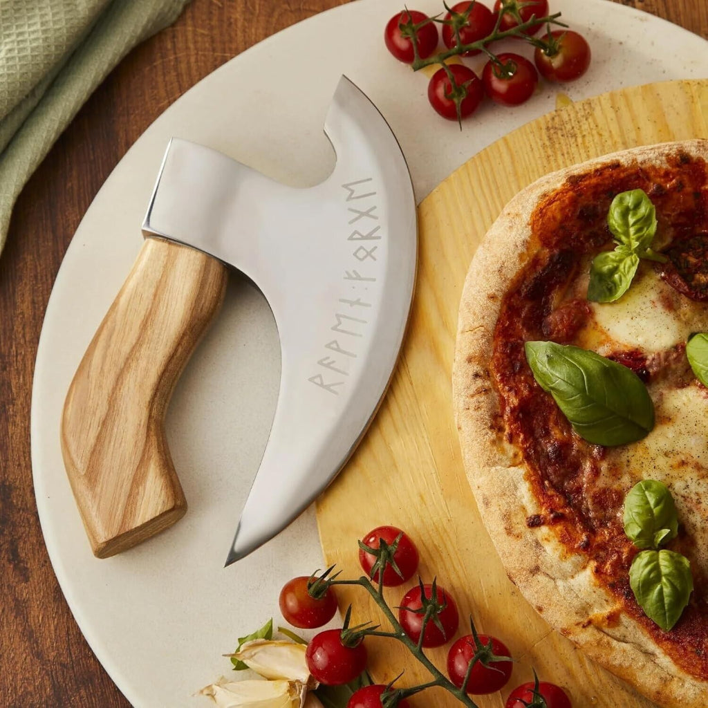 Wooden-handled cleaver on a cutting board with a pizza and tomatoes