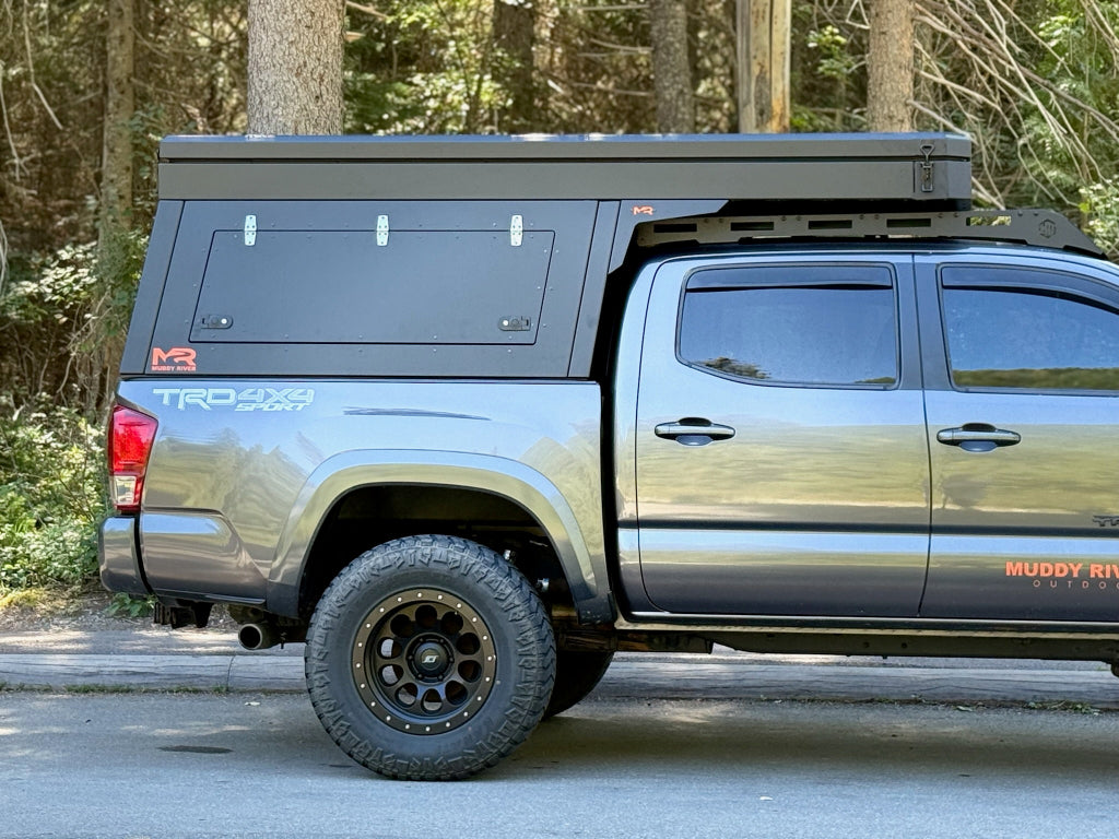 Right side view of a Eddy Topper Camper mounted to a gray 3rd generation Toyota Tacoma with trees in the background