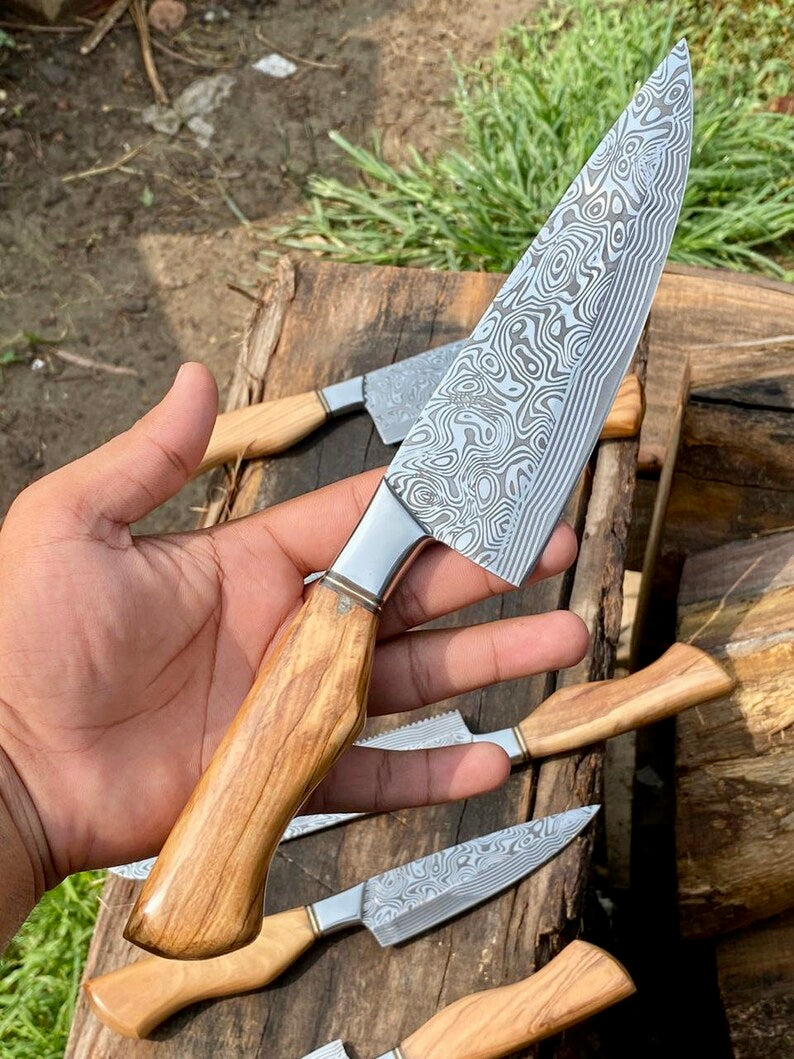 Hand holding a Damascus steel knife with wooden handle on a wooden surface