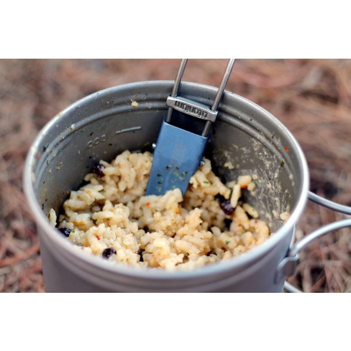 Camping pot with food and a spatula on a natural background