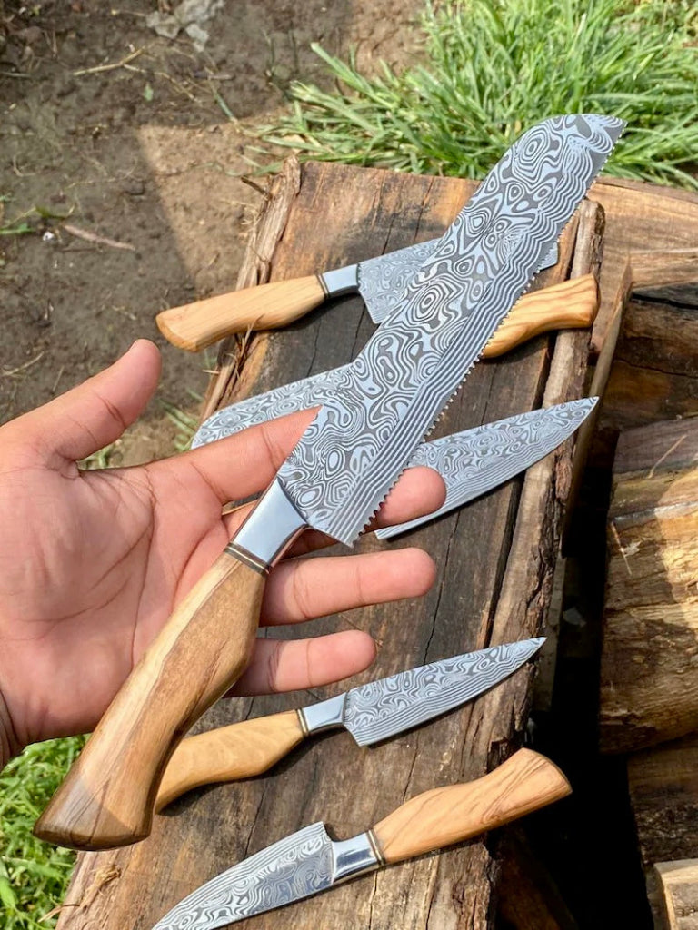 Set of Damascus steel knives with wooden handles on a wooden surface outdoors.