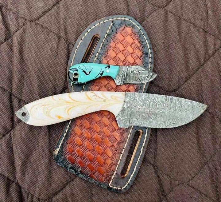 Two knives with decorative sheaths on a textured surface