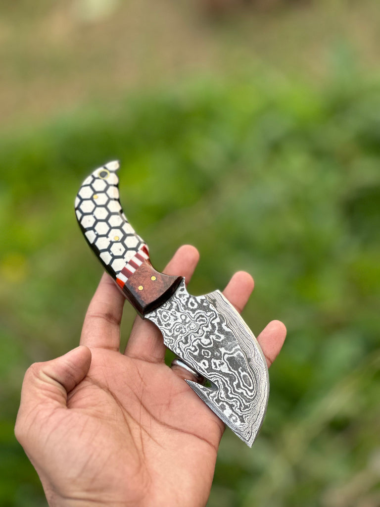 Hand holding a decorative knife with a unique blade design against a blurred green background
