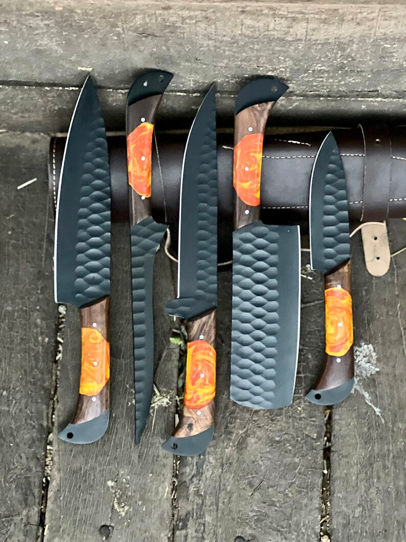 Set of five knives with black and orange handles on a wooden surface