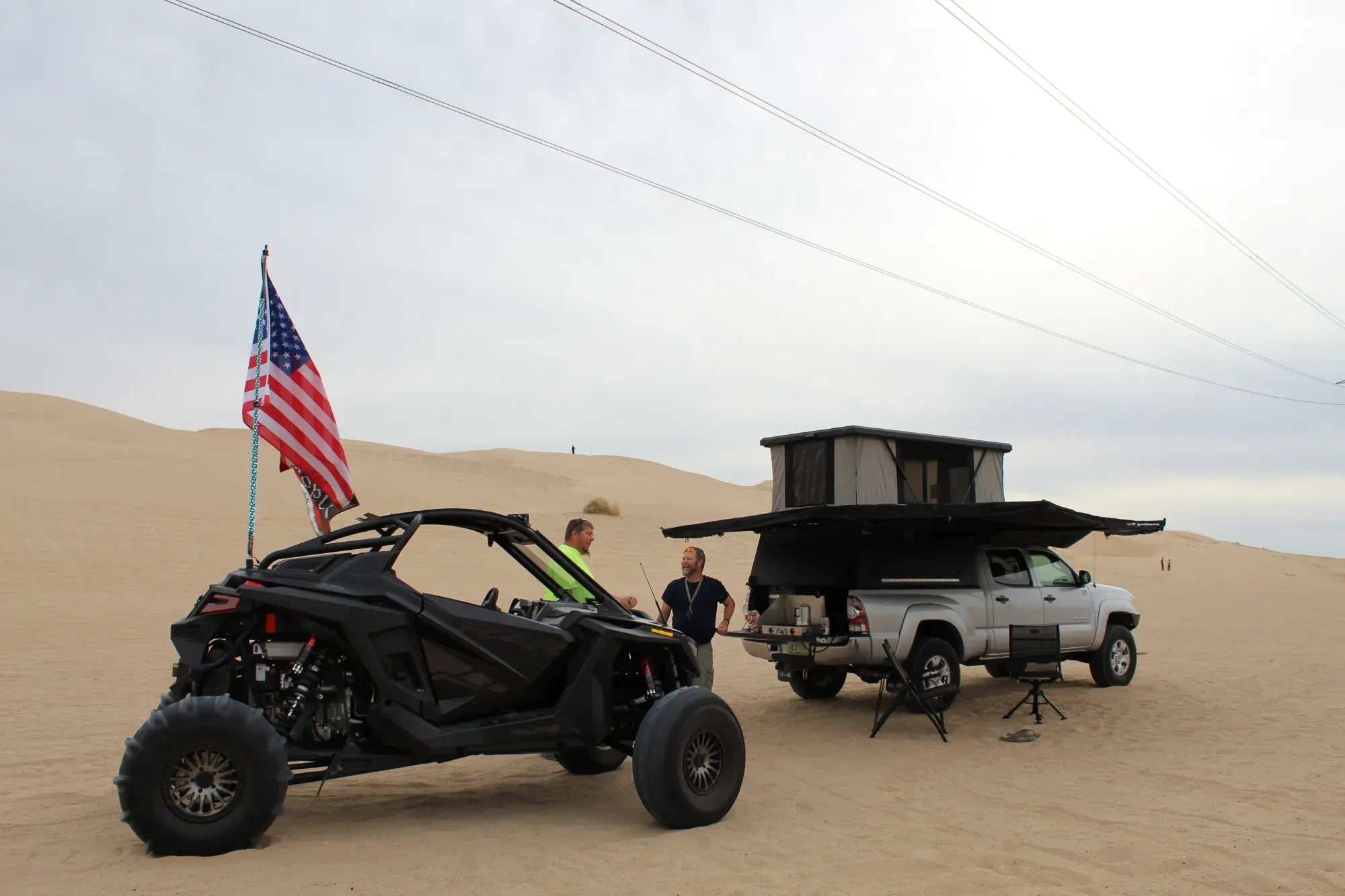 Dune buggy and truck with camper shell in sand dunes, American flag visible