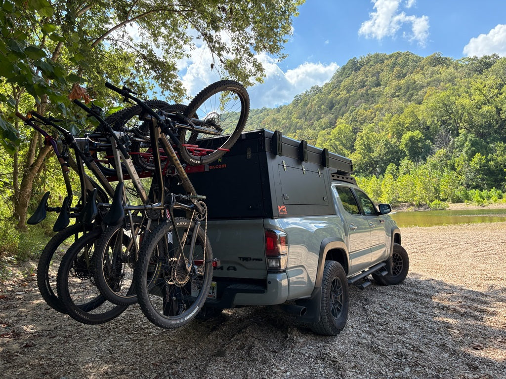 Truck with bicycles loaded on the back, surrounded by trees and a scenic landscape.